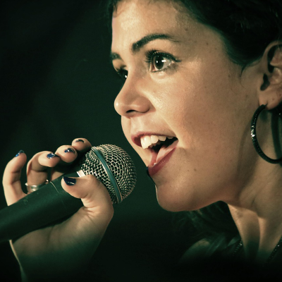 Photo d'une personne en train de chanter tenant un micro à la main. On aperçoit seulement une partie du visage, de la main et du micro.